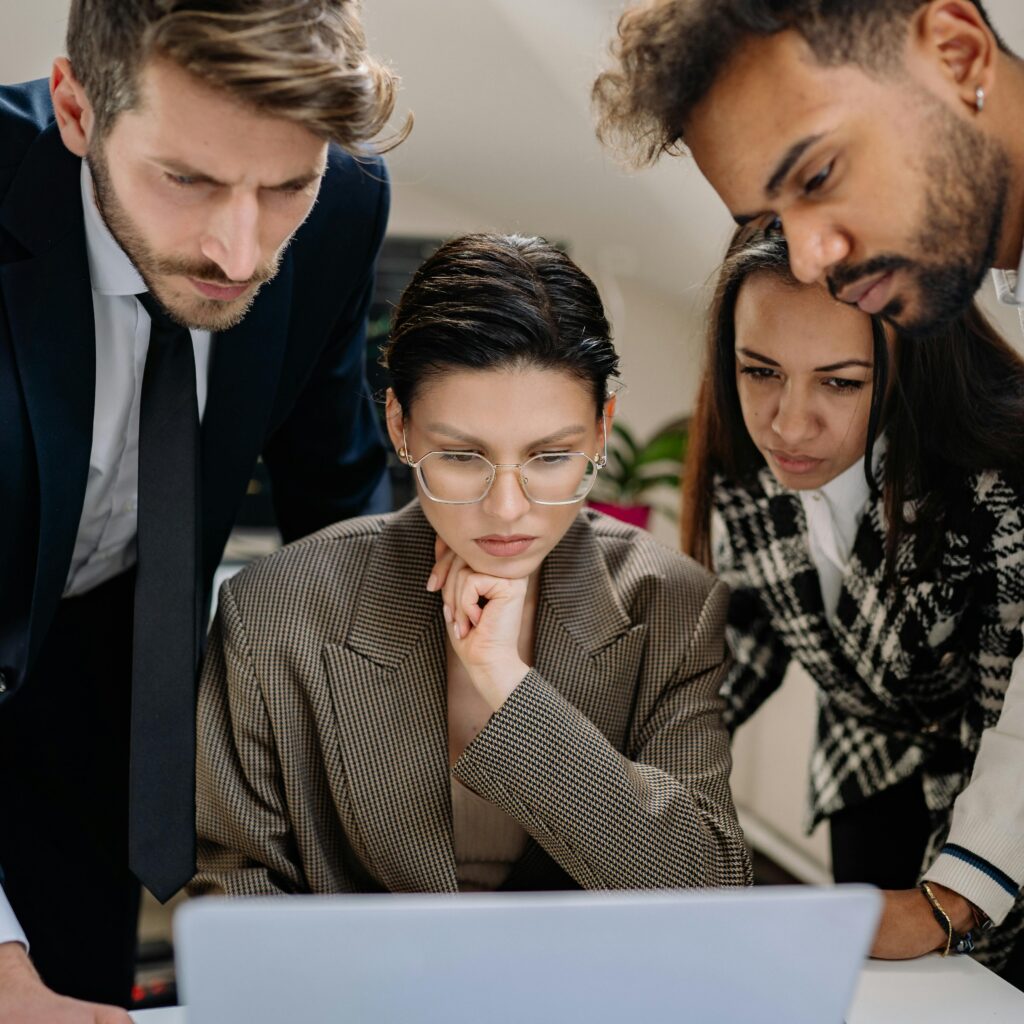 A diverse group of professionals intensely collaborating over a laptop indoors.